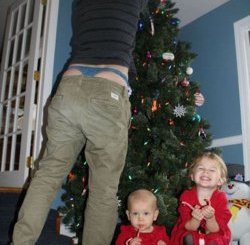 Tis the season to be slobby: A father reaches up to the Christmas tree and exposes more than what he had hoped for - as his two young children are oblivious to his antics